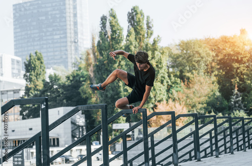 Doing parkour. Young man in sportive clothes have workout outdoors at daytime