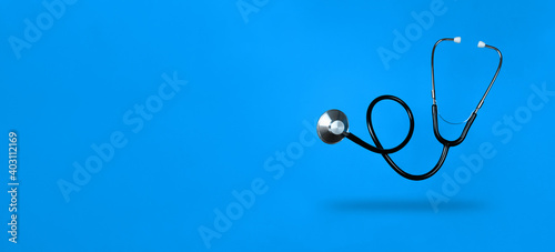 Levitating stethoscope on blue background and shadow under it with copy space. Stock photo.