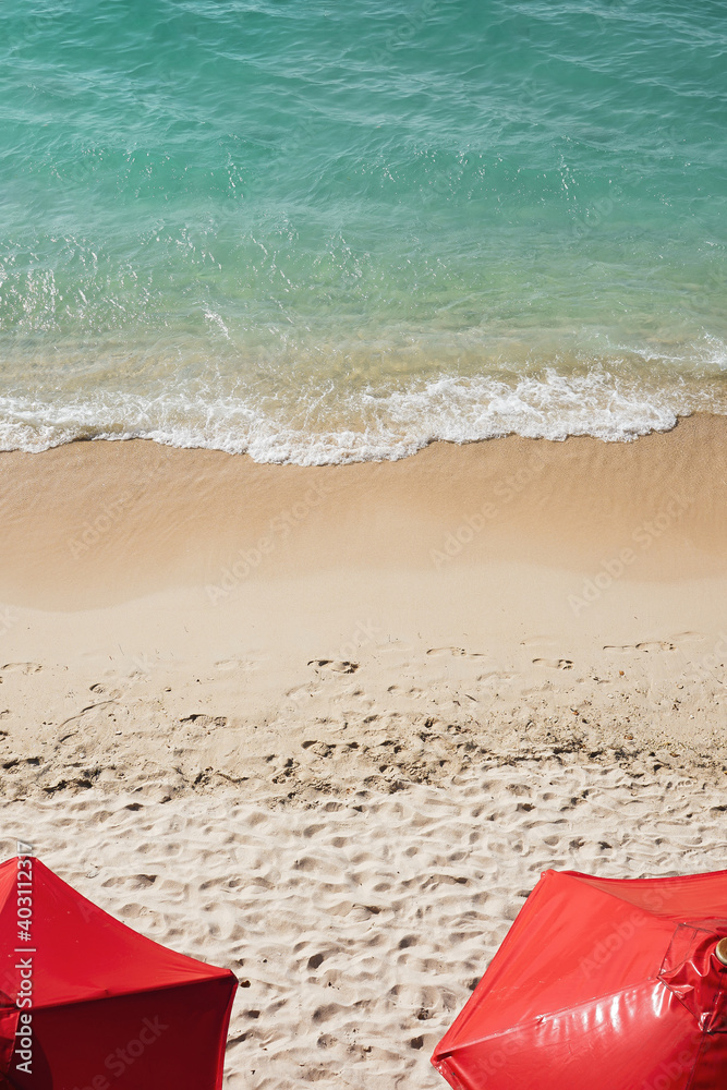 Toma cenital de hermosa playa caribeña con aguas turquesas en isla Colombiana junto a dos sombrillas rojas   
