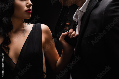 cropped view of dangerous woman holding gun near man in suit isolated on black
