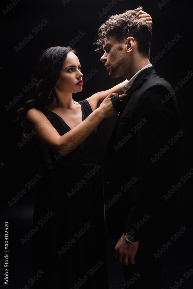 elegant woman with red lips looking at man and pulling hair on black