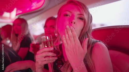 Beautiful women in the limousine clink glasses and drink champagne. Party with dances and colorful lights to music.