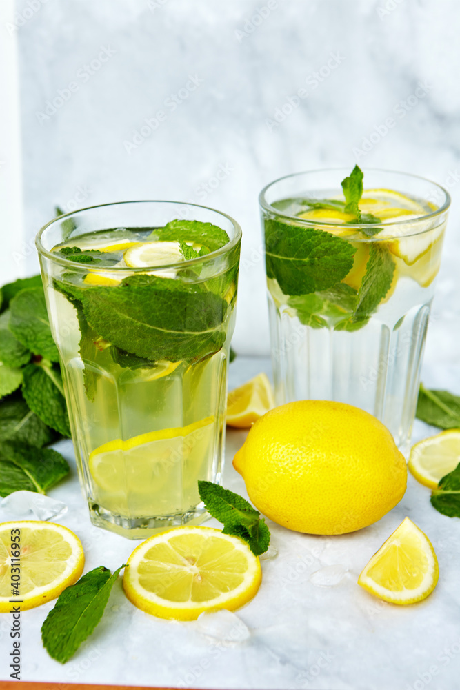 Refreshing drinks for summer, cold sweet and sour lemonade juice in the glasses with sliced fresh lemons. Refreshing summer drink. Traditional lemonade with lemon, mint and ice. Selective focus Refreshing drinks for summer, cold sweet and sour lemonade juice in the glasses with sliced fresh lemons. Refreshing summer drink. Traditional lemonade with lemon, mint and ice. Selective focus