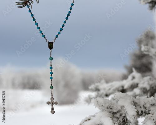 Rosary hanging in snowy evergreen tree © Kara
