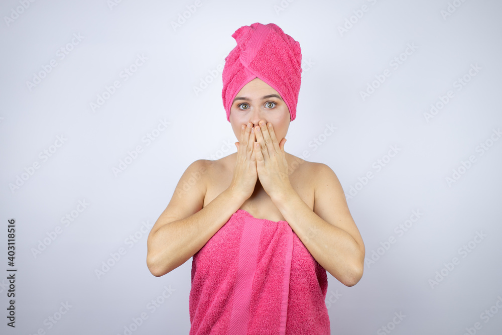 Young beautiful woman wearing shower towel after bath standing over isolated white background with her hands over her mouth and surprised Young beautiful woman wearing shower towel after bath standing over isolated white background with her hands over her mouth and surprised