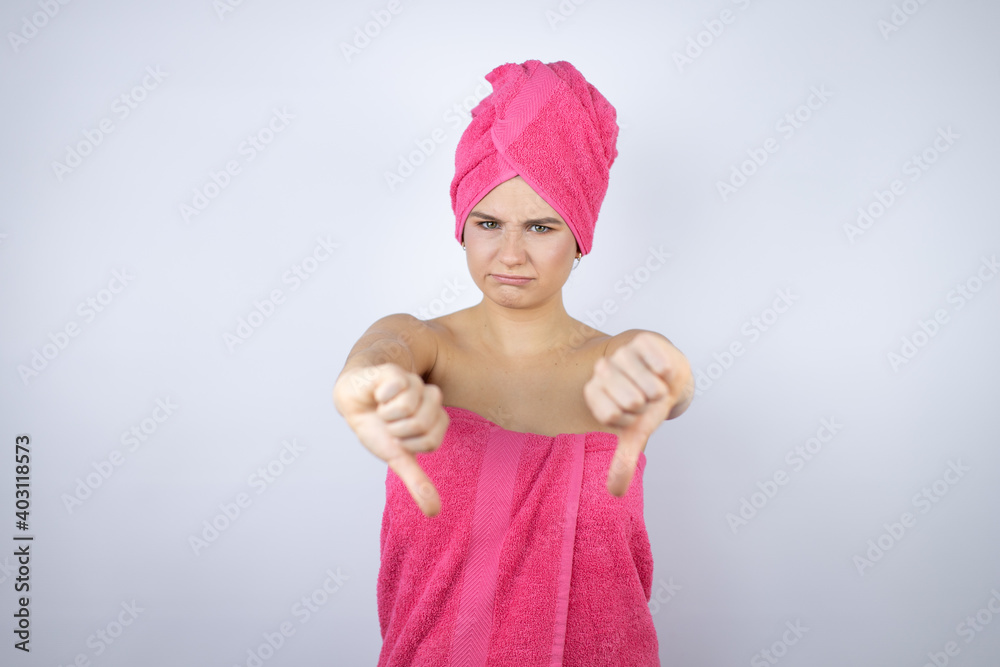 Young beautiful woman wearing shower towel after bath standing over isolated white background angry face, negative sign showing dislike with thumbs down Young beautiful woman wearing shower towel after bath standing over isolated white background angry face, negative sign showing dislike with thumbs down