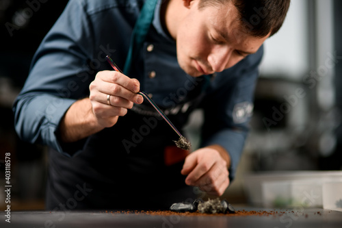 Close-up view on male chef holding tweezers with ingredient for preparing fusion cuisine dish