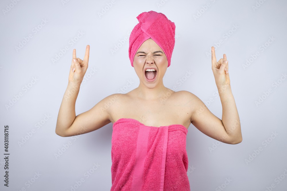 Young beautiful woman wearing shower towel after bath standing over isolated white background shouting with crazy expression doing rock symbol with hands up Young beautiful woman wearing shower towel after bath standing over isolated white background shouting with crazy expression doing rock symbol with hands up