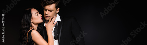 seductive woman touching face of boyfriend isolated on black, banner