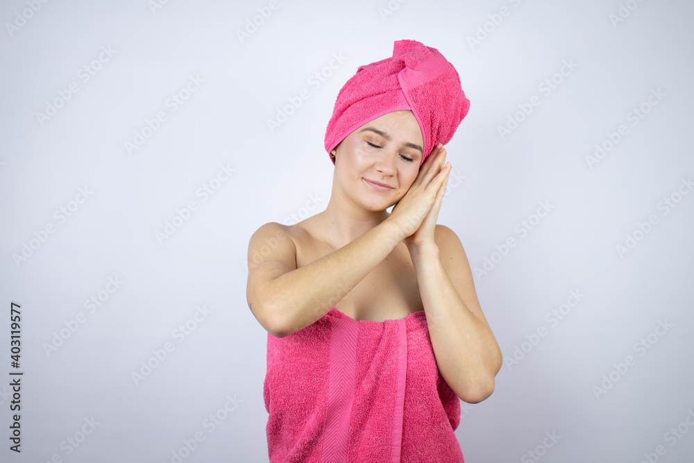 Young beautiful woman wearing shower towel after bath standing over isolated white background sleeping tired dreaming and posing with hands together while smiling with closed eyes. Young beautiful woman wearing shower towel after bath standing over isolated white background sleeping tired dreaming and posing with hands together while smiling with closed eyes.