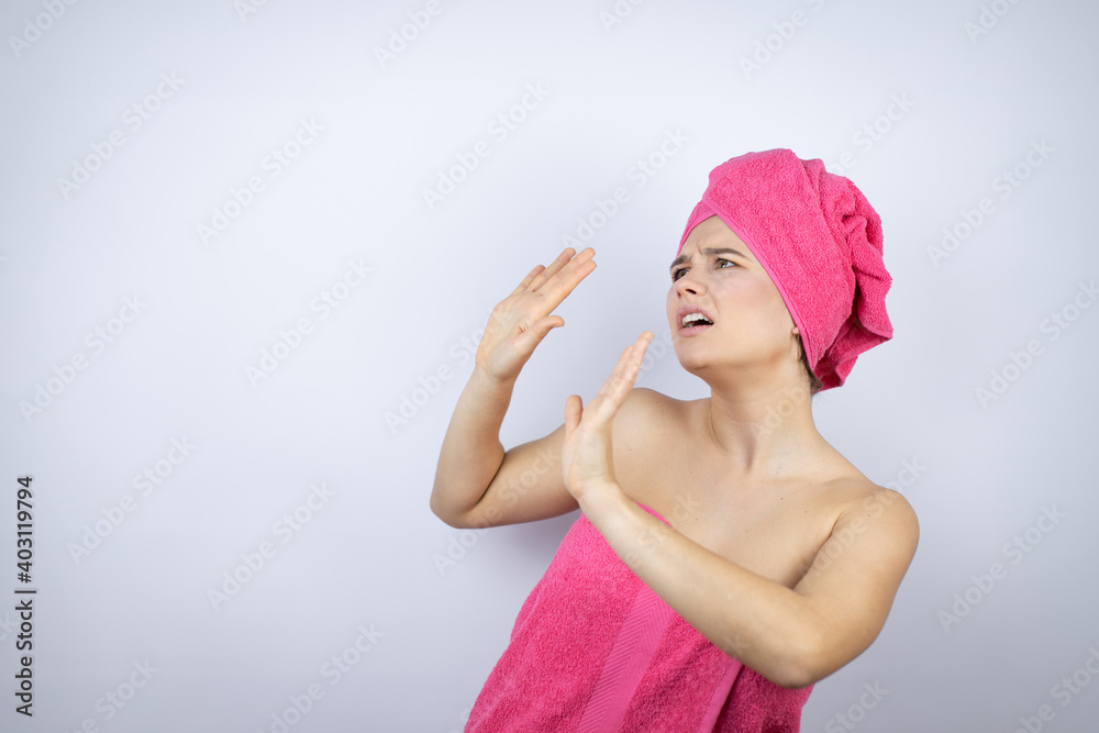 Young beautiful woman wearing shower towel after bath standing over isolated white background scared with her arms up like something falling from above Young beautiful woman wearing shower towel after bath standing over isolated white background scared with her arms up like something falling from above