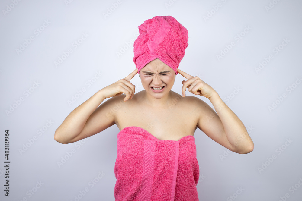 Young beautiful woman wearing shower towel after bath standing over isolated white background covering ears with fingers with annoyed expression for the noise of loud music. Deaf concept. Young beautiful woman wearing shower towel after bath standing over isolated white background covering ears with fingers with annoyed expression for the noise of loud music. Deaf concept.