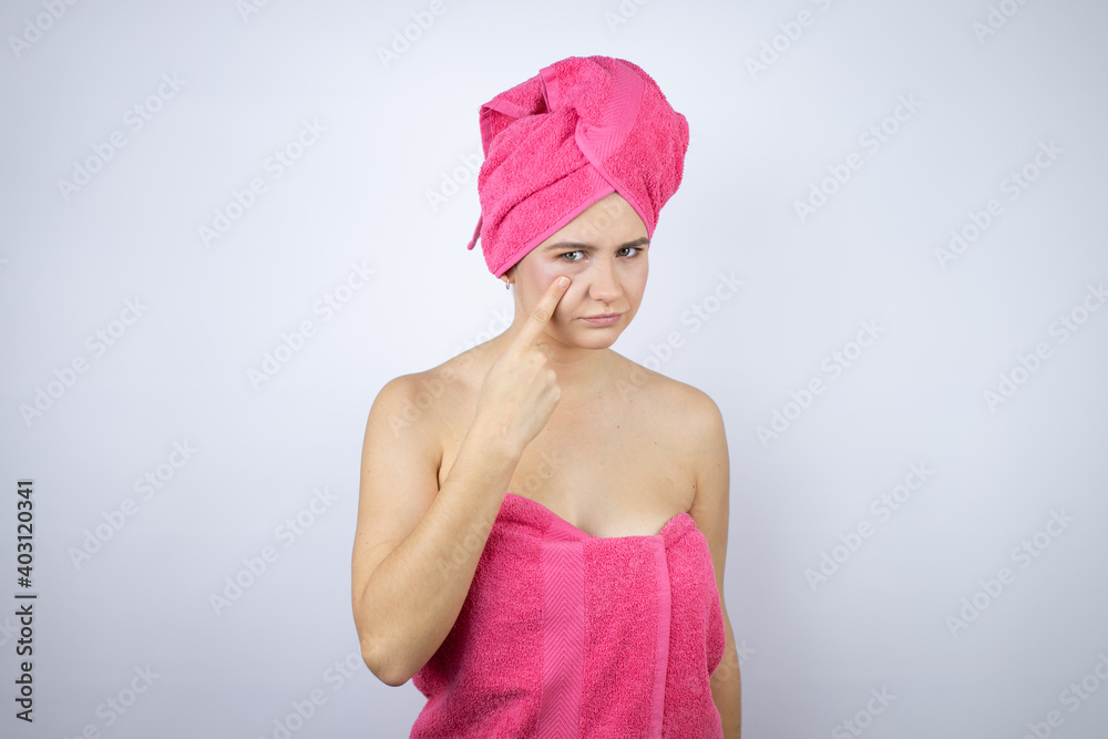 Young beautiful woman wearing shower towel after bath standing over isolated white background Pointing to the eye watching you gesture, suspicious expression