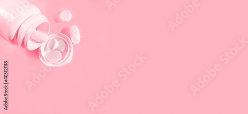 Medical pills spilling out of a drug bottle over pink background. Medical concept.