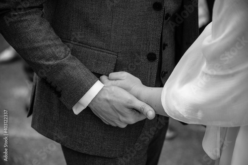 Closeup black and white photo of bride and groom holding their hands gently, elegantly dressed.