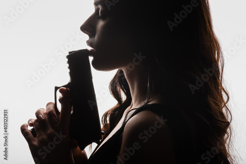 Obraz na plátně side view of brunette young woman with closed eyes holding gun isolated on white