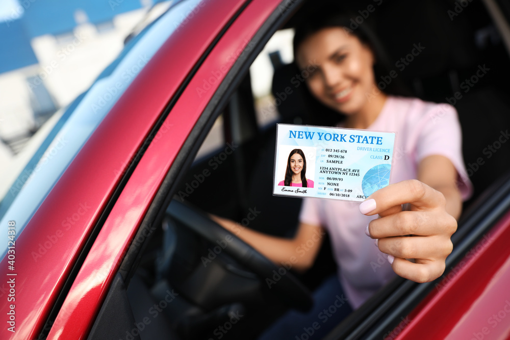 Happy young woman holding license while sitting in car, focus on hand. Driving school