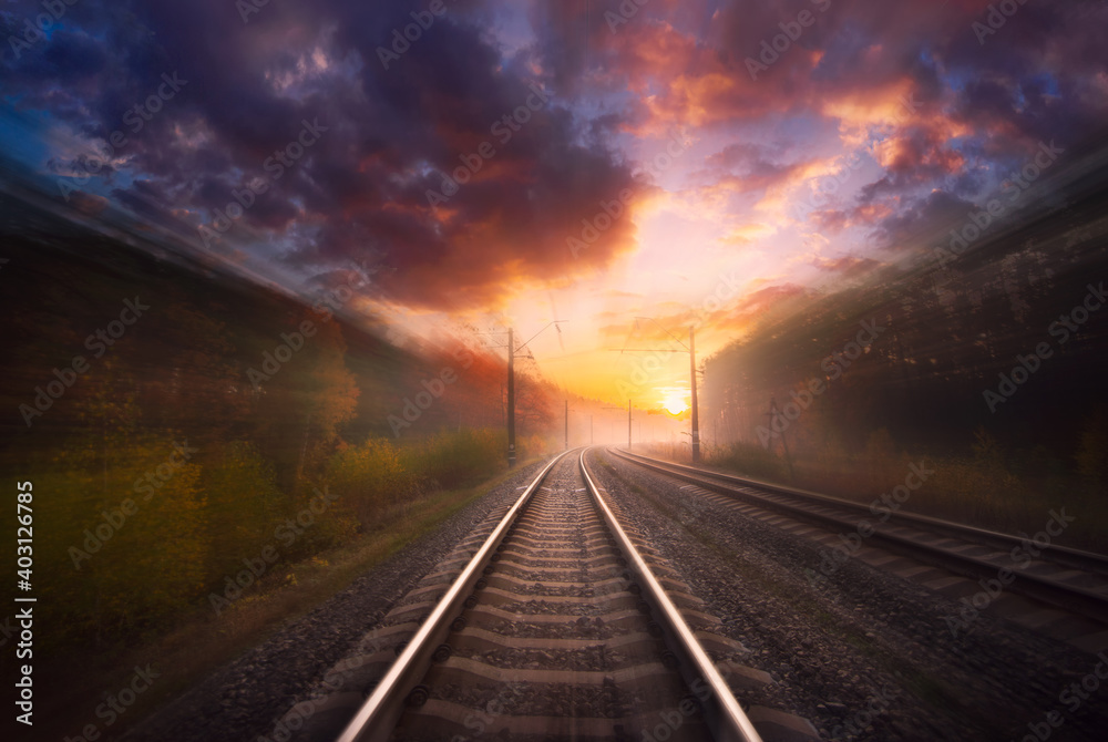 Railway in motion at sunset with blur effect. Train travels by rail in the forest with dramatic sky. Railway in motion at sunset with blur effect. Train travels by rail in the forest with dramatic sky.