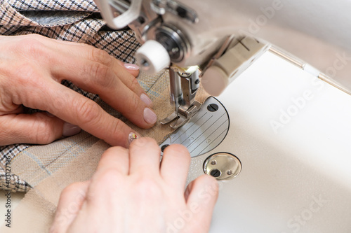 Woman hand guiding white cloth through a sewing machine. Close-up view.