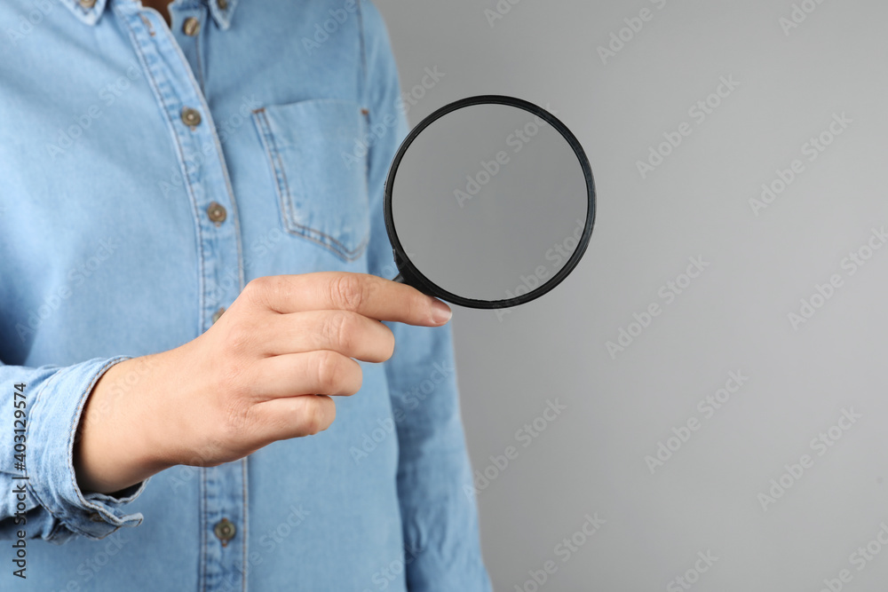 Woman holding magnifying glass on grey background, closeup. Find keywords concept Woman holding magnifying glass on grey background, closeup. Find keywords concept