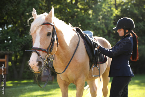 Young woman in horse riding suit and her beautiful pet outdoors on sunny day