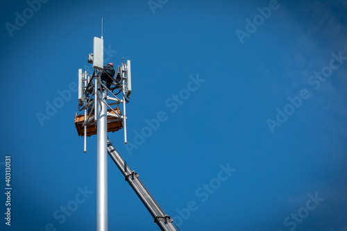 Workers install cellular base station with transmitters 3G, 4G, 5G and antennas on cell tower on background of blue sky. Mobile telecommunication equipments