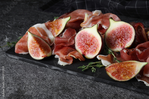 Delicious ripe figs and prosciutto served on slate board, closeup