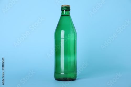 Glass bottle with water on light blue background