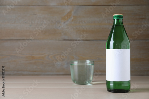Bottle and glass with water on wooden table, space for text