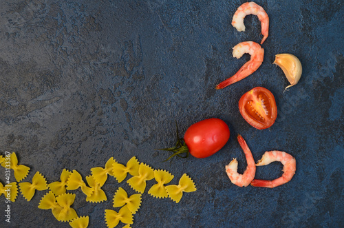 Culinary or food background on a dark concrete table. Pasta bows farfale, cherry tomatoes, garlic and shrimp, ingredients for making of pasta with seafood with recipe photo