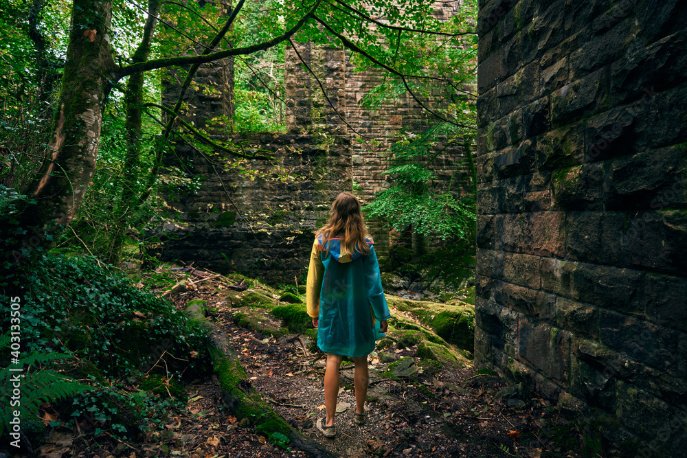 Young woman walking in forest by stone wall
