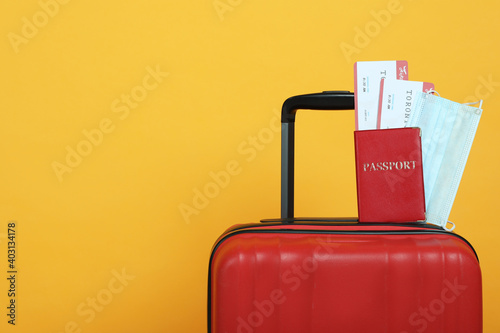 Passport with tickets and protective mask on suitcase against yellow background, space for text. Travel during quarantine