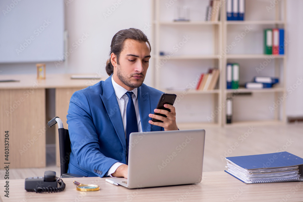 Young male employee in wheel-chair working in the office Young male employee in wheel-chair working in the office