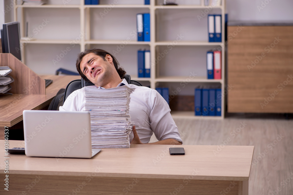 Young male employee unhappy with excessive work in the office Young male employee unhappy with excessive work in the office