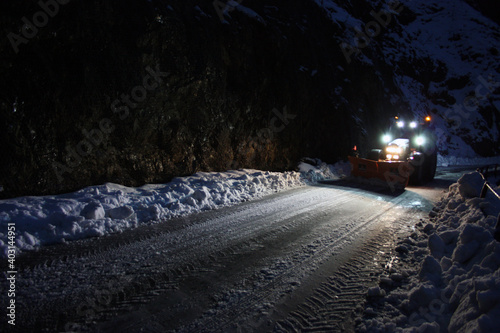snowplow passes through the snowy mountain streets in the evening to clean up the road traffic © Alessia