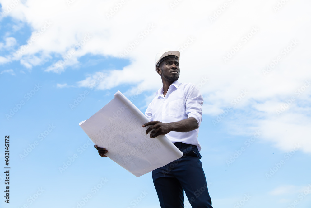 african american businessman in protective safety hard hat looking at blueprint plans on construction site. african american businessman in protective safety hard hat looking at blueprint plans on construction site.