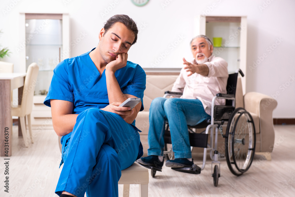 Old man in wheel-chair and young bad caregiver indoors