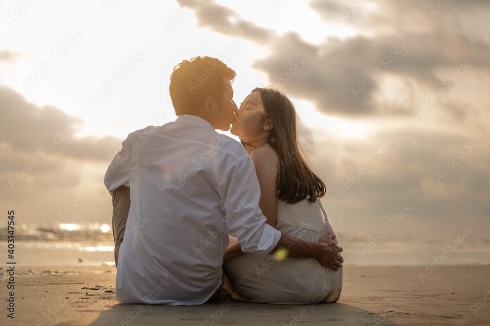 Young couple kissing and sit on the beach in the sunset.Summer in love,Valentine day concept. Young couple kissing and sit on the beach in the sunset.Summer in love,Valentine day concept.