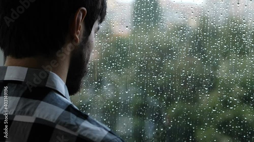 solitude, depression - young sad man looks out the window in a rainy day photo