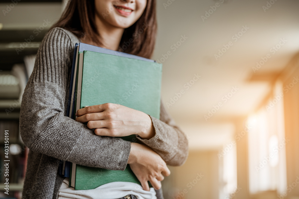 Asian woman standing behind her is a bookshelf in a university library..Concept of education, school, library and knowledge.. Asian woman standing behind her is a bookshelf in a university library..Concept of education, school, library and knowledge..
