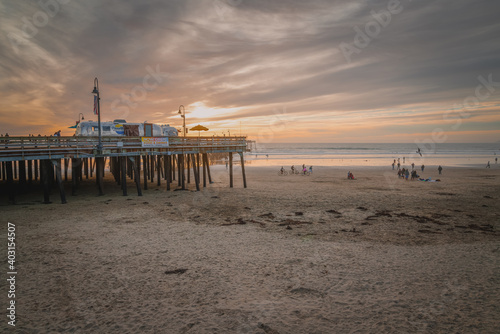  Sunset on Pismo Beach, California. An old wooden pier, sandy beach, and people enjoying ocean view