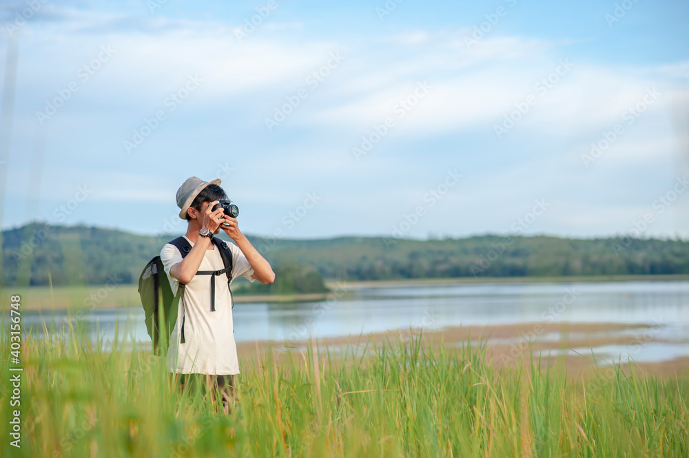 Young Asian man traveler wearing knitted hat with backpack taking a photo at amazing lake. Young Asian man traveler wearing knitted hat with backpack taking a photo at amazing lake.