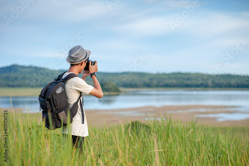 Young Asian man traveler wearing knitted hat with backpack taking a photo at amazing lake.