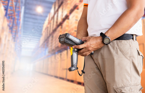 Warehouse supervisor holding barcode scanner. Inventory management cargo on tall shelves. Warehousing and Logistics.