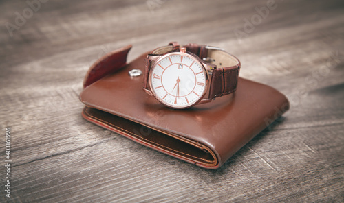 Brown wristwatch and wallet on the wooden background.