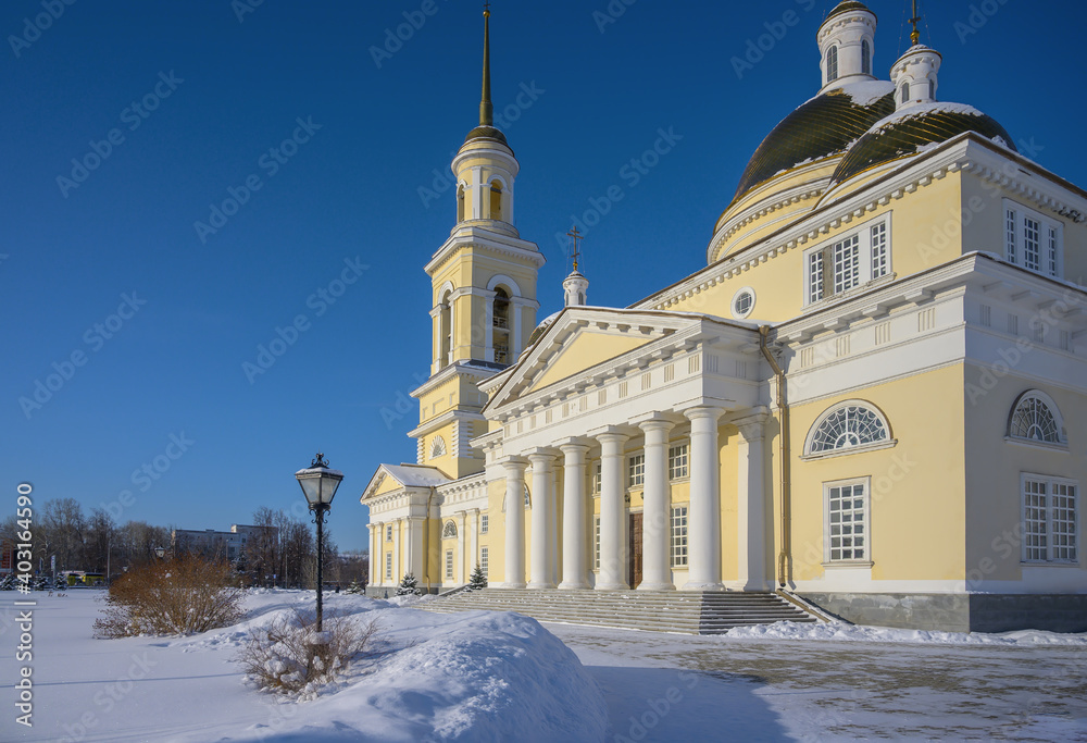 church in the snow. a majestic stone Orthodox church with a bell tower, white columns, white-yellow domes in the historical center of Nevyansk (Russia). winter sunny day, blue sky, a lot of white snow