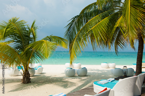  White sand beach and turquoise ocean palm leaves and modern white rattan furniture. Relaxing sea landscape