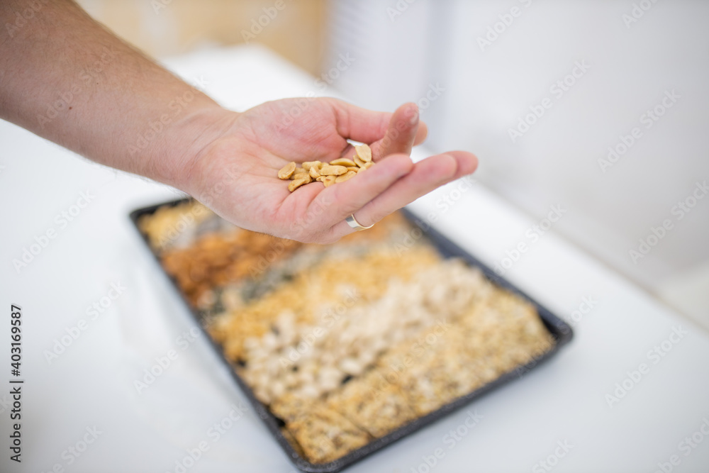 Male hand holding peanuts above a black tray with seeds and nuts Male hand holding peanuts above a black tray with seeds and nuts