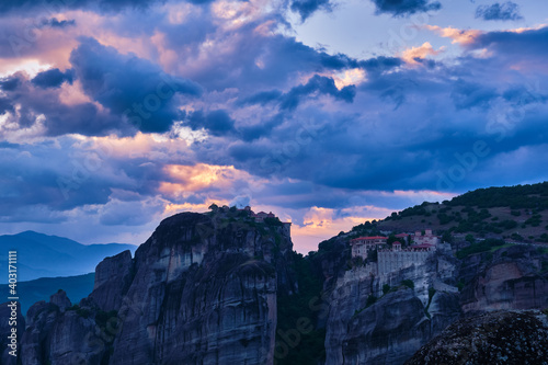 Twilight over Varlaam and Great Meteoron monasteries in Meteora, Greece. Underexposed, great sunset with clouds and sun rays. UNESCO World Heritage