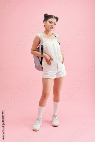 Fashionable young girl wears holding backpack, posing isolated on pink background.